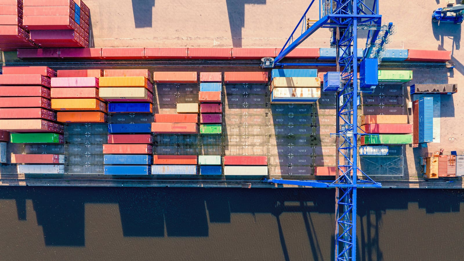 Containers stacked alongside a quay with a gantry crane over the berth